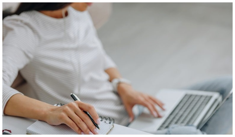 An online student watching a course on their laptop with a notebook and pen to take notes