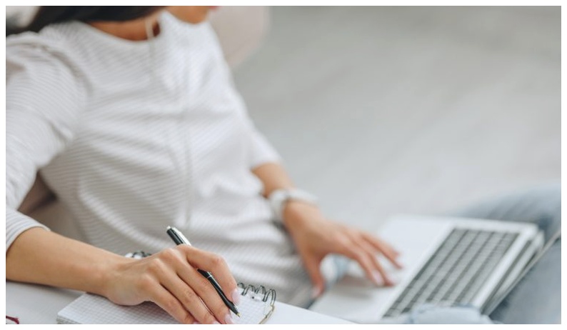 An online student watching a course on their laptop with a notebook and pen to take notes
