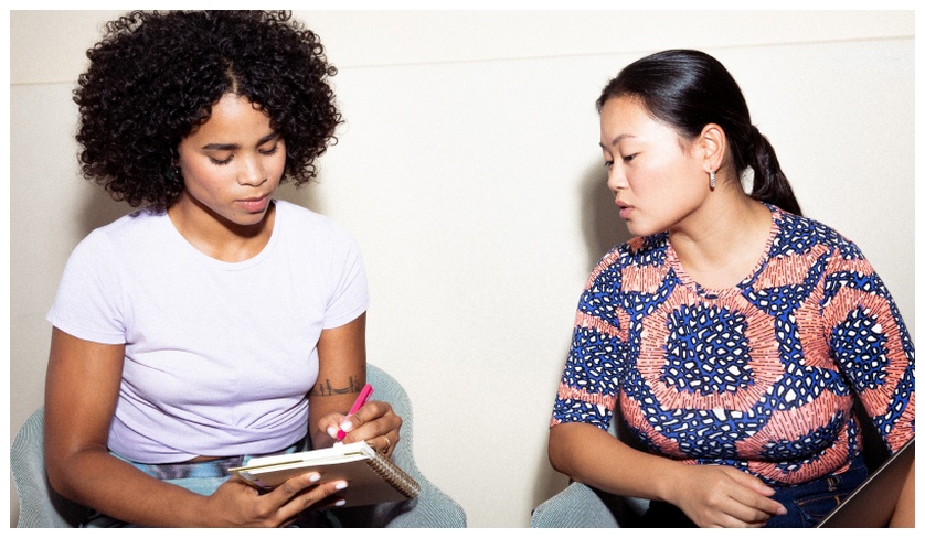 2 women chatting and taking notes